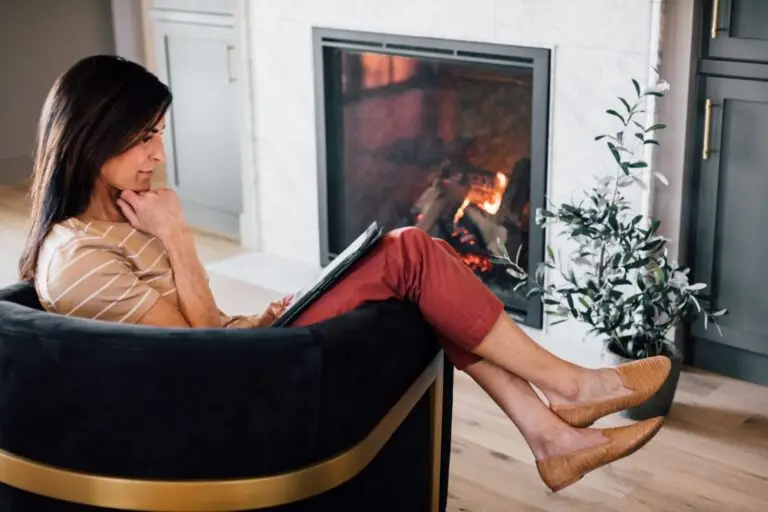 Woman relaxing in front of a gas fireplace staying warm & reading her iPad.