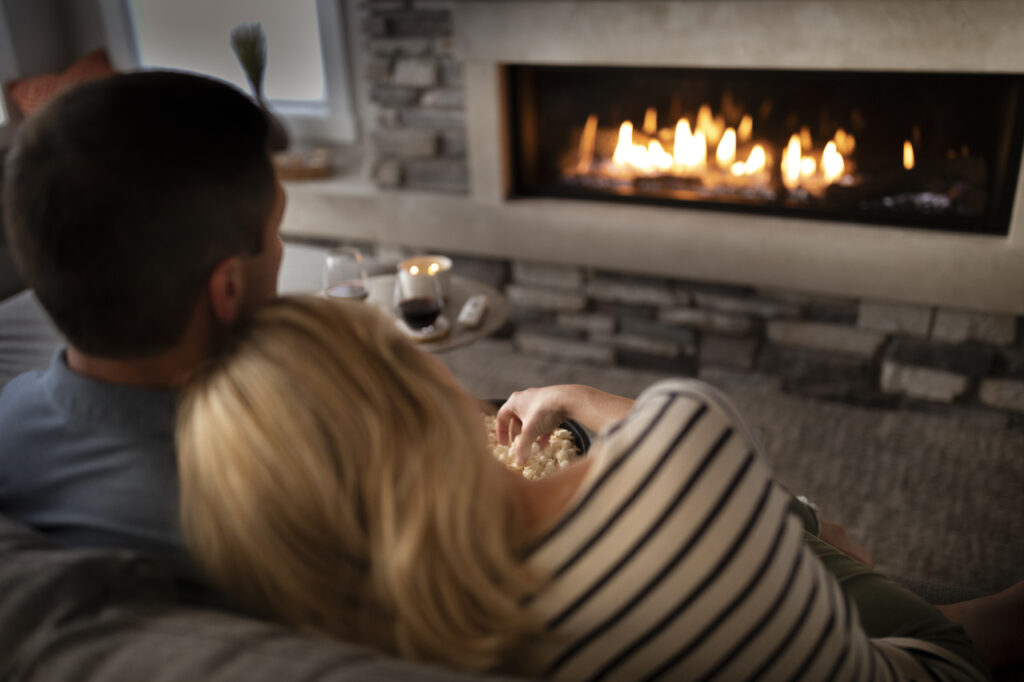 Couple eating popcorn and enjoying their linear gas fireplace together in living room.